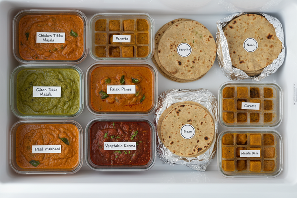 Organized freezer shelf with labeled Indian food containers — curries, parathas in foil, and masala base in ice cube trays for batch cooking"